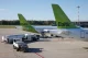 Two Baltic airplanes with bright green tails parked at a sunlit gate, ground equipment nearby.