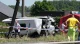 White van with severe front-end damage at a crash site, responders and investigators behind red-and-blue tape.