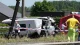 White van with severe front-end damage at a crash site, responders and investigators behind red-and-blue tape.