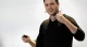 Male presenter with a headset microphone, holding a remote and gesturing with a raised fist during a talk.