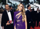 Woman in a purple sequined gown posing on a red carpet with guests and photographers in the background.