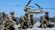 US Army soldiers in camouflage gear kneeling on snowy ground as a CH-47 Chinook helicopter hovers nearby in a mountainous area.