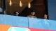 Four spectators stand behind a blue glass railing in a stadium box, watching an event.