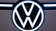 Close-up of a glowing Volkswagen circular logo on a car, dark background around it.
