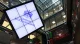 Large screen displaying the London Stock Exchange logo in a modern trading floor with scrolling ticker boards nearby.