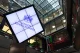 Large screen displaying the London Stock Exchange logo in a modern trading floor with scrolling ticker boards nearby.