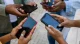 Group of friends standing in a circle, each holding a smartphone and looking at their screens in a casual outdoor setting.