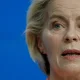 Close-up of a woman speaking, set against a solid blue background.