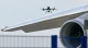 Quadcopter drone hovering near the wing and engine of a large commercial airplane at an airport.