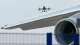 Quadcopter drone hovering near the wing and engine of a large commercial airplane at an airport.