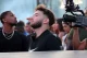 Man with short beard in a black Nike shirt looks to the side as a cameraman films nearby at a crowded event
