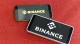 Two smartphones displaying the Binance logo on a red surface